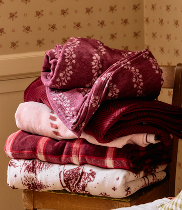 Stack of folded blankets in burgundy and cream with floral and plaid patterns displayed on wooden chair.3