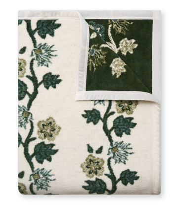 Woven blanket with dark green vine and leaf pattern on cream and dark green sides, white binding edges.