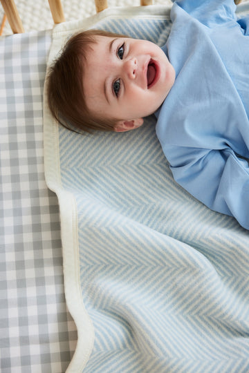 Infant wrapped in light blue herringbone patterned blanket on a crib with checkered bedding.6