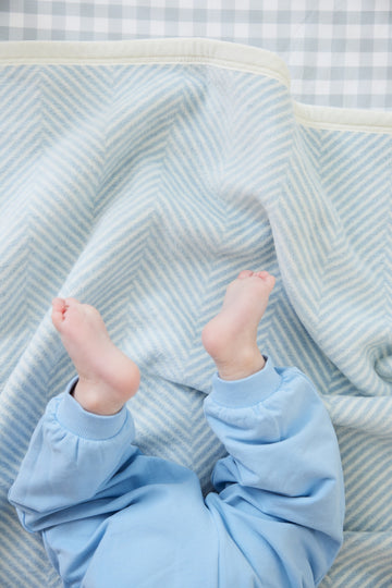 Light blue and white herringbone patterned mini blanket with cream binding, draped over infant's legs.2