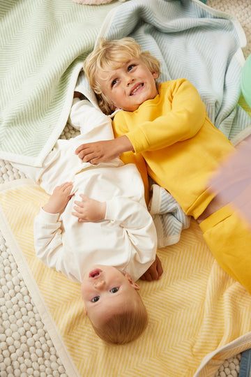 Butter yellow herringbone blanket with white trim, displayed with two children on a neutral-toned floor.5