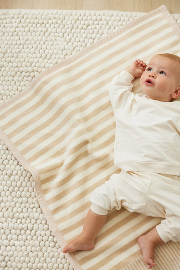 Infant on textured cream blanket with beige and white stripes, placed on knitted surface.6