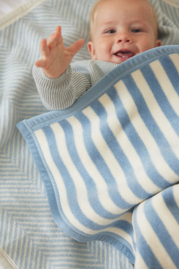 Baby wrapped in blue and cream striped blanket with geometric patterned background.8