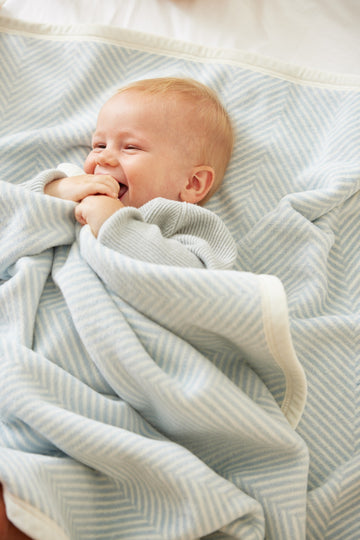 Infant wrapped in light blue and cream herringbone patterned blanket.5