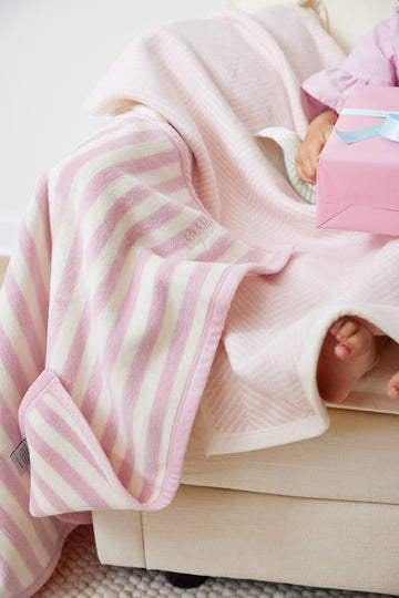 Ballet pink and cream herringbone striped mini blanket draped over a person holding a pink box.6