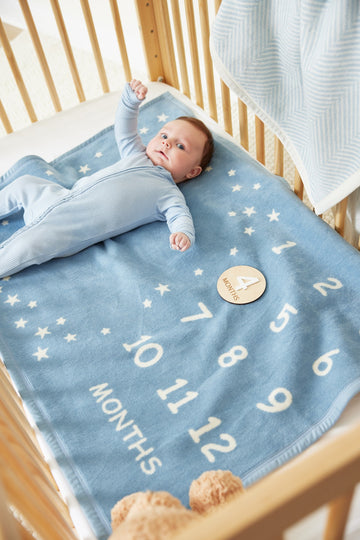 Infant in striped pajamas lying on light blue blanket with white stars and month numbers in wooden crib.5
