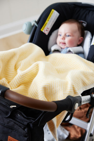 Butter yellow herringbone patterned mini blanket draped over a stroller with an infant inside.6