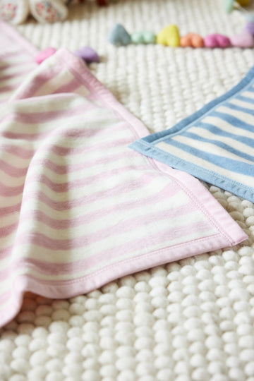 Pink and white striped mini blanket folded on textured surface with blue striped blanket nearby.5