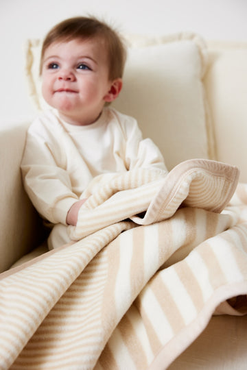 Cream and beige striped mini blanket draped over toddler sitting in chair.2