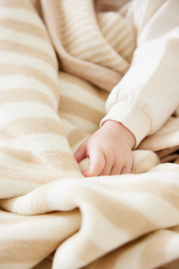 Baby's hand resting on beige and cream striped knit blanket with matching sweater visible.4