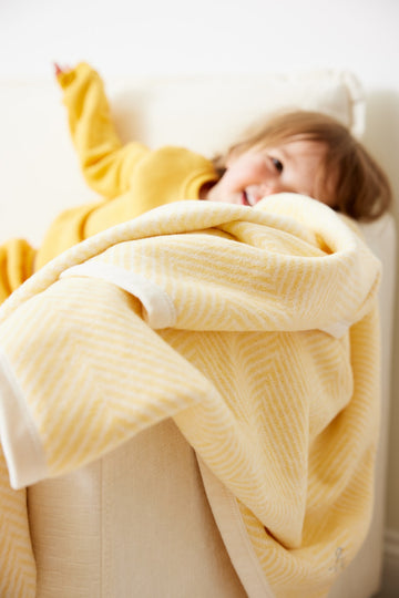 Butter yellow mini blanket with herringbone weave pattern, draped over a toddler in yellow clothing.2