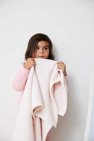 Child holding pale pink herringbone-textured mini blanket with white and pink coloring.5