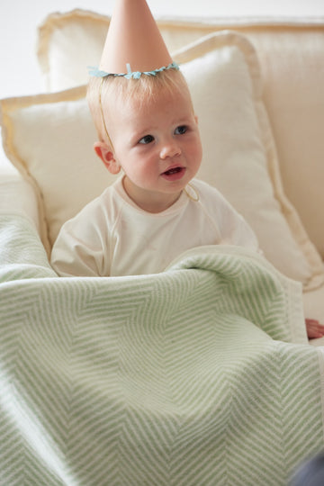 Infant wrapped in sprout green herringbone patterned blanket sitting on cream couch.2