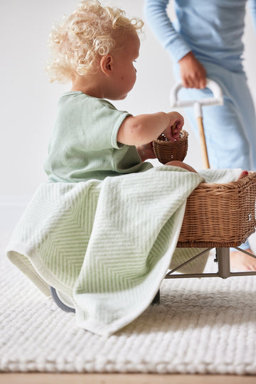 Sprout green herringbone mini blanket with cream trim draped over toddler in wicker basket.6