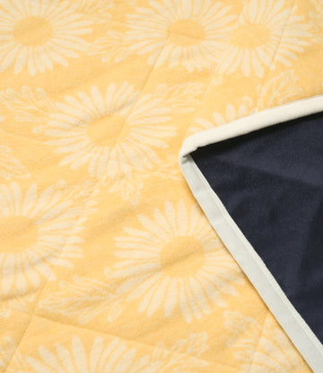 Yellow outdoor blanket with daisy pattern, white binding edge, and dark navy reverse side visible.9