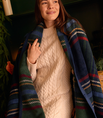 Tartan blanket in navy, green, red, and gold plaid worn draped over shoulders by a woman in a cream cable-knit sweater.5
