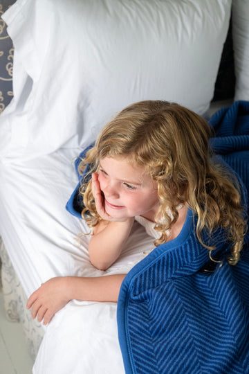 Child resting on white pillow and blue herringbone patterned blanket.4