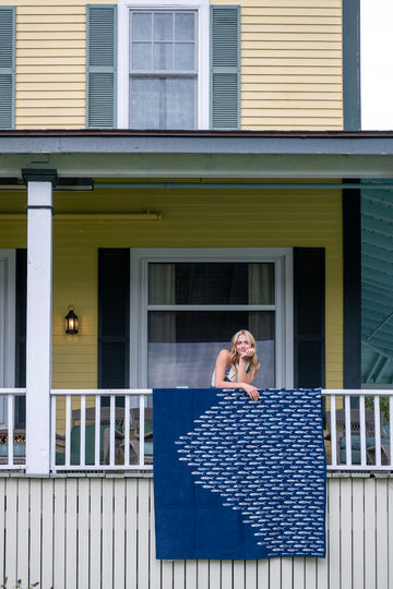 Navy blue blanket with white fish pattern displayed on a porch railing.3