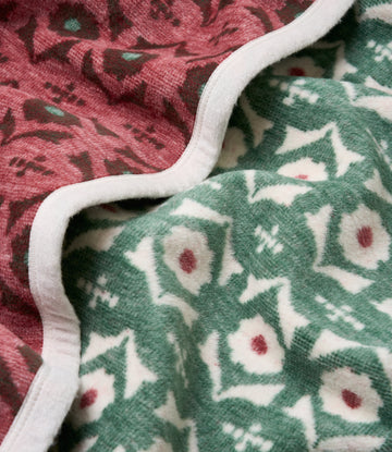 Folded blanket with pink and green floral patterns, white binding edge, textured knit fabric visible.8