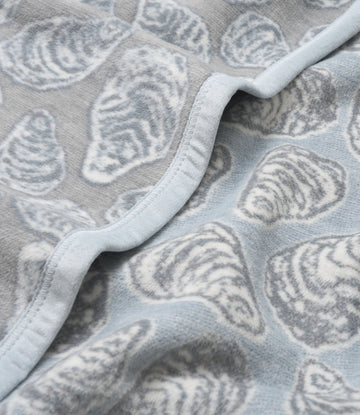 Gray and white shell-patterned blanket with white binding and curved edge detail.7