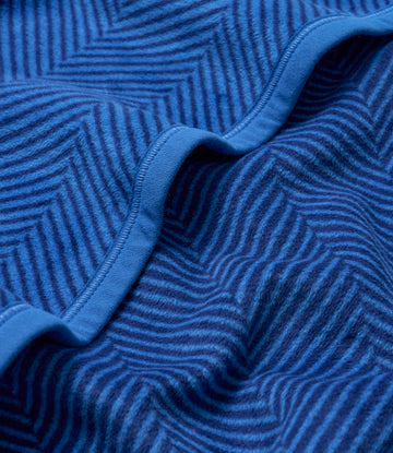 Blue blanket with herringbone weave pattern and bound edges, shown folded to display texture detail.