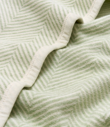 Folded blanket with sprout green and cream herringbone weave pattern and binding edge detail.4