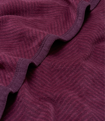 Plum-colored blanket with herringbone weave pattern and stitched binding along folded edges.4