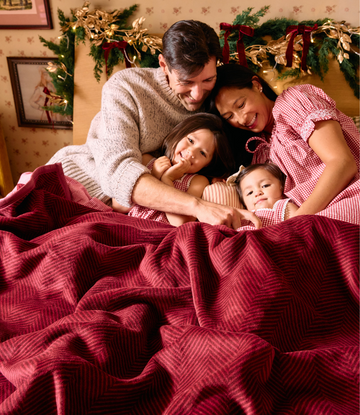 Cranberry herringbone textured blanket draped over a family of four on a bed.3