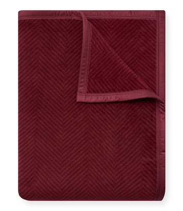 Cranberry-colored blanket with herringbone weave pattern and bound edges, partially folded.