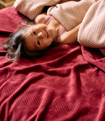 Child resting on cranberry and beige herringbone patterned blankets with ribbed texture.2