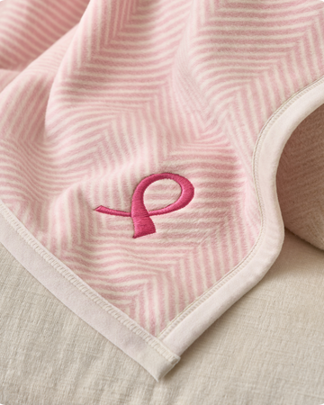 Pink herringbone patterned fabric with embroidered magenta ribbon symbol and white trim edge.