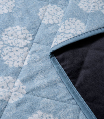 Blue and white patterned outdoor blanket with quilted texture and dark backing visible at edge.8