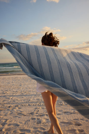 Light blue and white striped blanket with geometric tile pattern held by person on beach.4