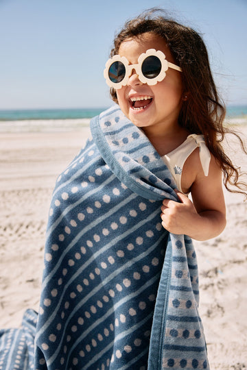 Child wrapped in blue and white patterned blanket with geometric dot design at the beach.4
