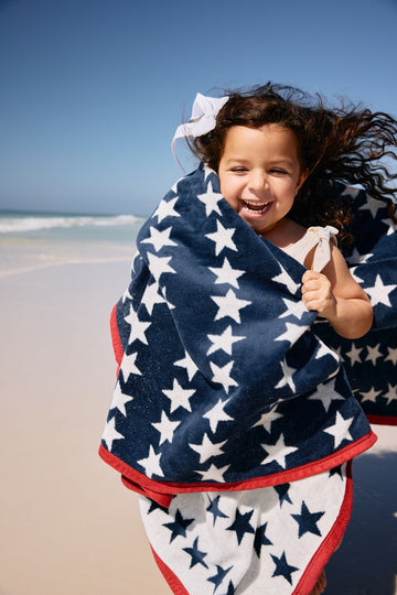 Navy and white star patterned blanket with red trim, draped around child at beach.8