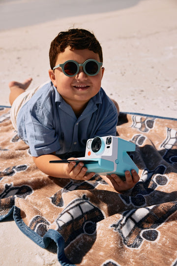 Tan and navy patterned midi blanket with wagon design, displayed on beach sand.2