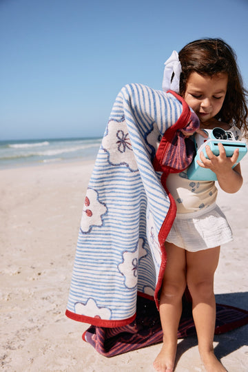 Blue and white striped blanket with cherry print and red trim worn by child at beach.5