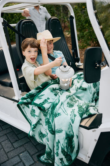 Green and white fish-patterned blanket draped over two children sitting in a golf cart.2