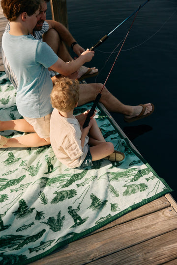 Cream and green blanket with fish and plant print used by man and child fishing on a dock.7