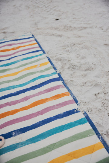 Striped outdoor blanket with multicolored horizontal bands laid on sand at a beach.5