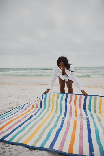Multicolored striped outdoor blanket with blue border spread on beach sand near ocean.6
