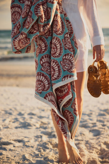 Turquoise blanket with burgundy shell pattern and cream border draped over person at beach.2