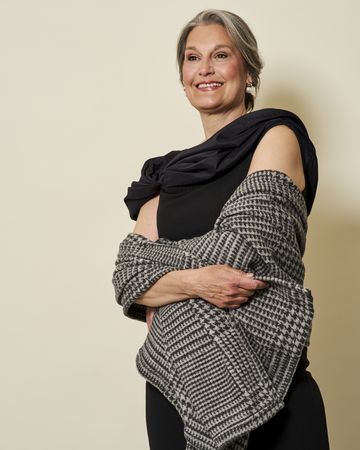 Woman wearing a gray and white houndstooth plaid shawl draped over her shoulders with a black sleeveless top.4