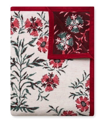 Folded blanket with cream base featuring red floral motifs and green leaves, bordered in deep red trim.