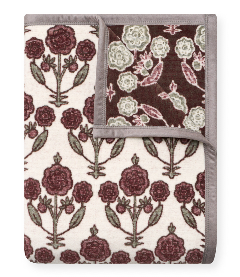 Folded blanket with blockprint floral design in burgundy, cream, and sage on cream and dark backgrounds, gray binding.