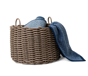 Woven rope basket in tan with two rope handles, containing folded blue striped and patterned fabrics.4