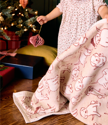 Cream blanket with red puppy faces draped over child's lap near Christmas tree.5