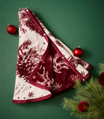 Red and cream toile tree skirt with Santa and forest scenes, featuring snap closures and decorative trim.3