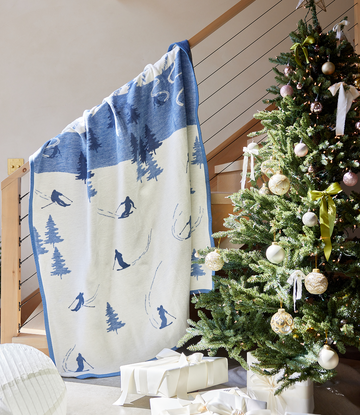 Blue and cream blanket with ski and tree motifs draped over a railing next to a decorated Christmas tree.4