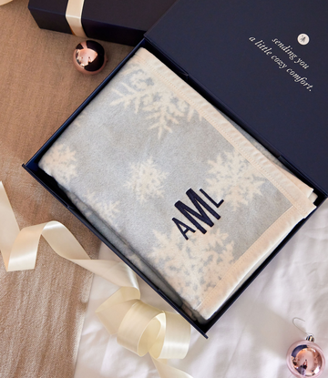 Cream and gray blanket with snowflake pattern and "AMI" text, displayed in navy gift box with ribbon.6